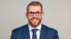 Adam Hagedorn, Managing Director at BGO, wearing a blue suit and glasses against a neutral background.