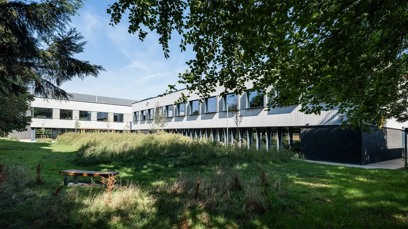 Exterior view of The Press in Foxton, Cambridge, featuring modern lab and office buildings surrounded by landscaped green space and mature trees.